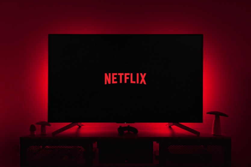 Telewizor, na którego ekranie wyświetla się napis netflix, widziany na czerwonym tle