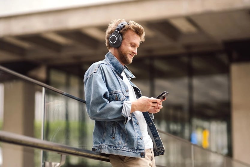 mężczyzna w słuchawkach audio-technica ATX50xBT2 uśmiecha się do telefonu